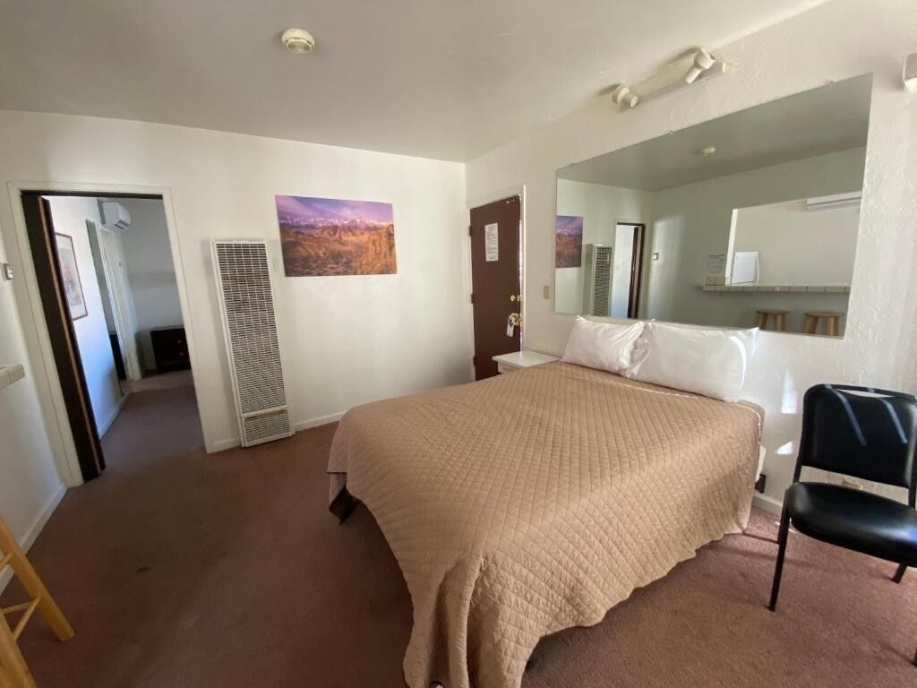 A bedroom with a bed, a chair, a mirror, a door, and a hallway.