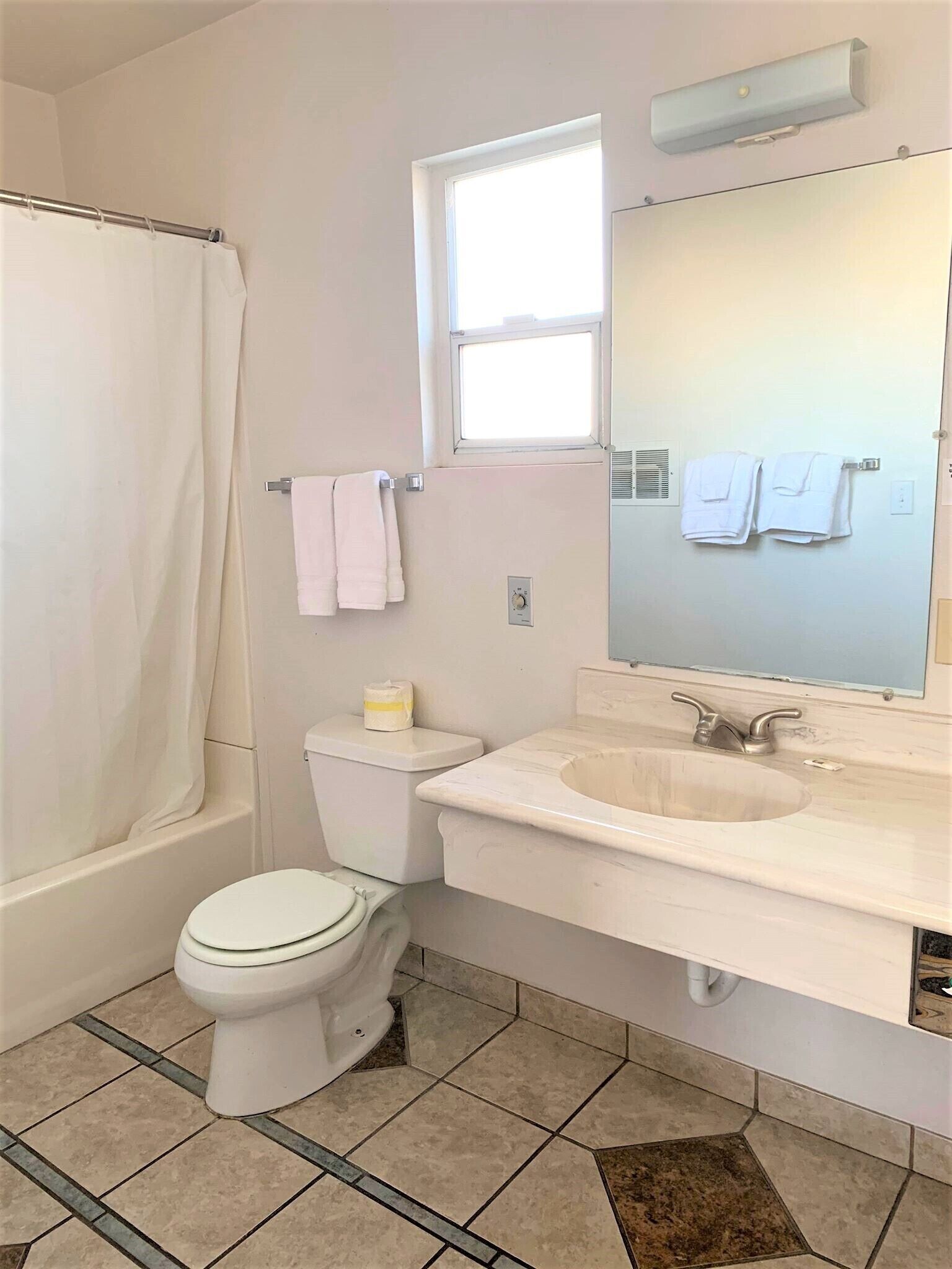 A bathroom with a bathtub, toilet, sink, and a window above the mirror.