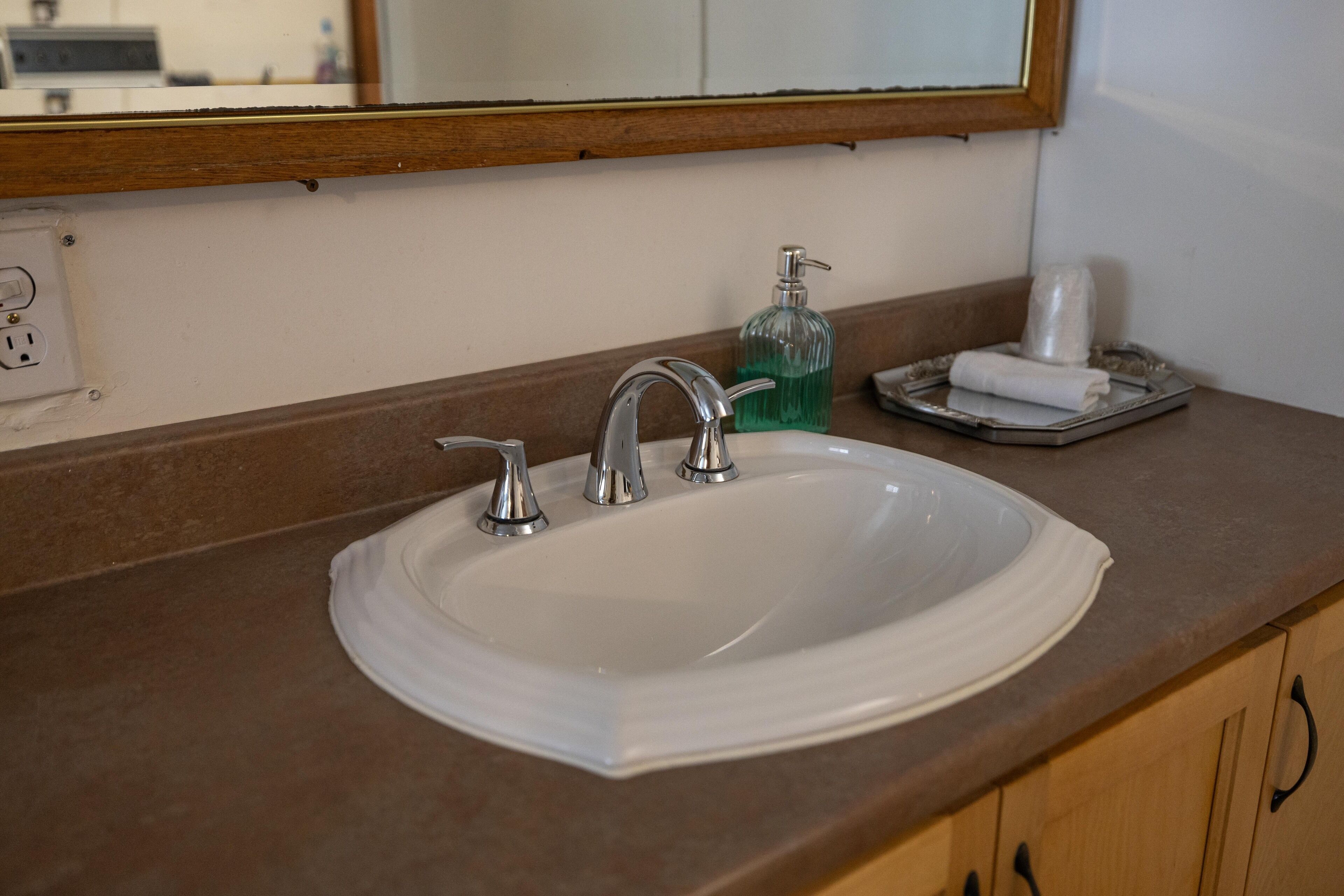 A bathroom sink with a mirror above it, a soap dispenser, and a towel on a tray.