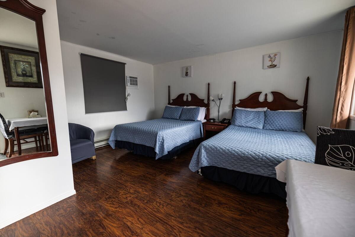 Hotellihuone, jossa on kaksi erillistä sänkyä, puulattia, työpöytä tuolilla sekä suuri peili.