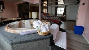 Una habitación con una bañera grande, un espejo y una cama con almohadas.