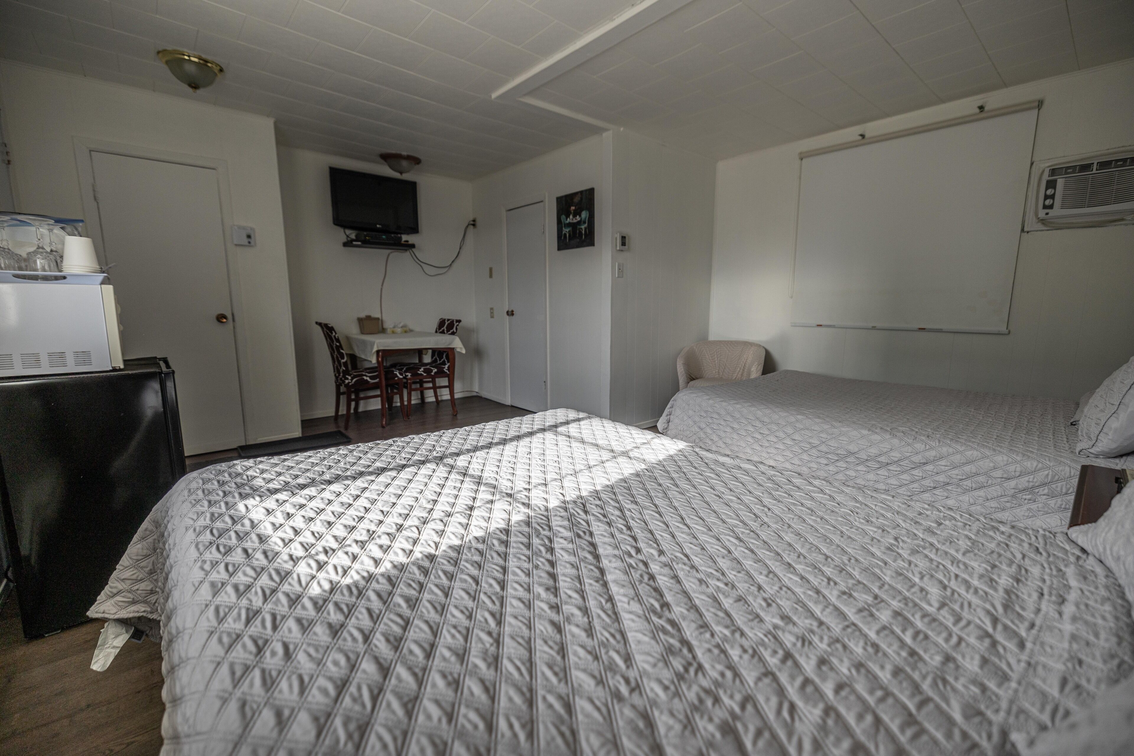 A hotel room with two beds, a desk with a chair, a television mounted on the wall, and a whiteboard.