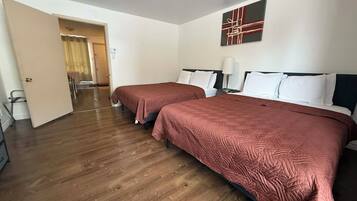 A hotel room with two beds, wooden flooring, a door leading to a hallway, and a painting on the wall.