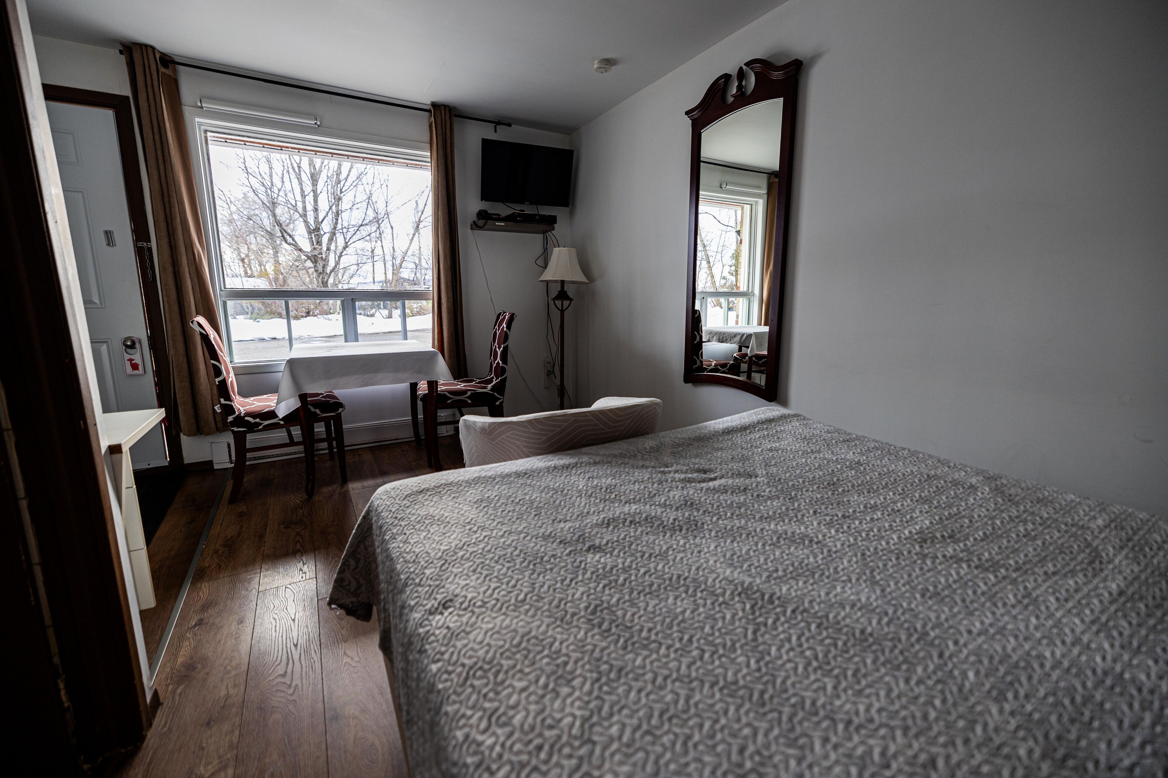 Une chambre d’hôtel avec un grand lit, une chaise, un bureau, un téléviseur fixé au mur et une fenêtre avec des rideaux.