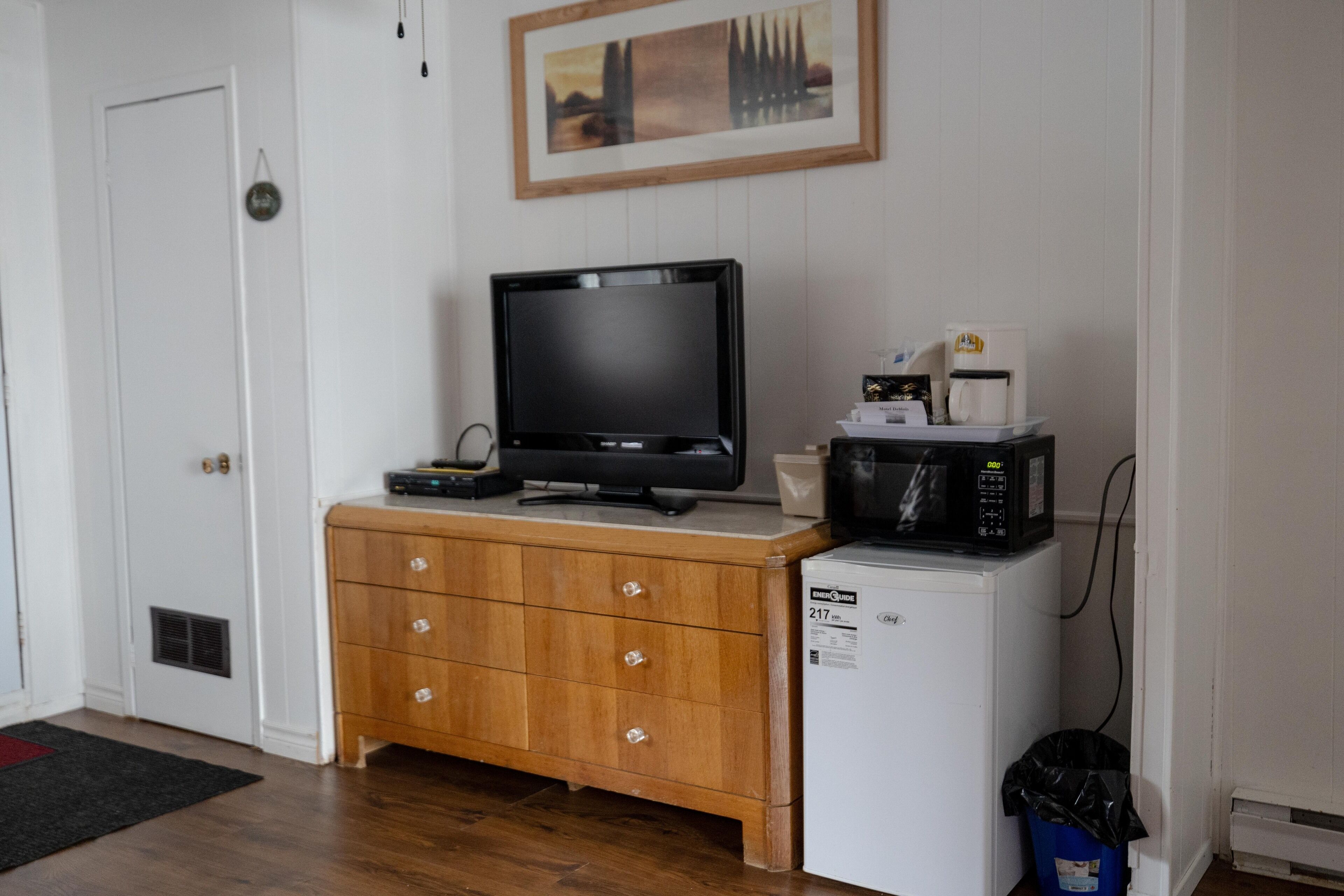 A compact kitchenette with a microwave, coffee maker, and a television on a wooden cabinet.