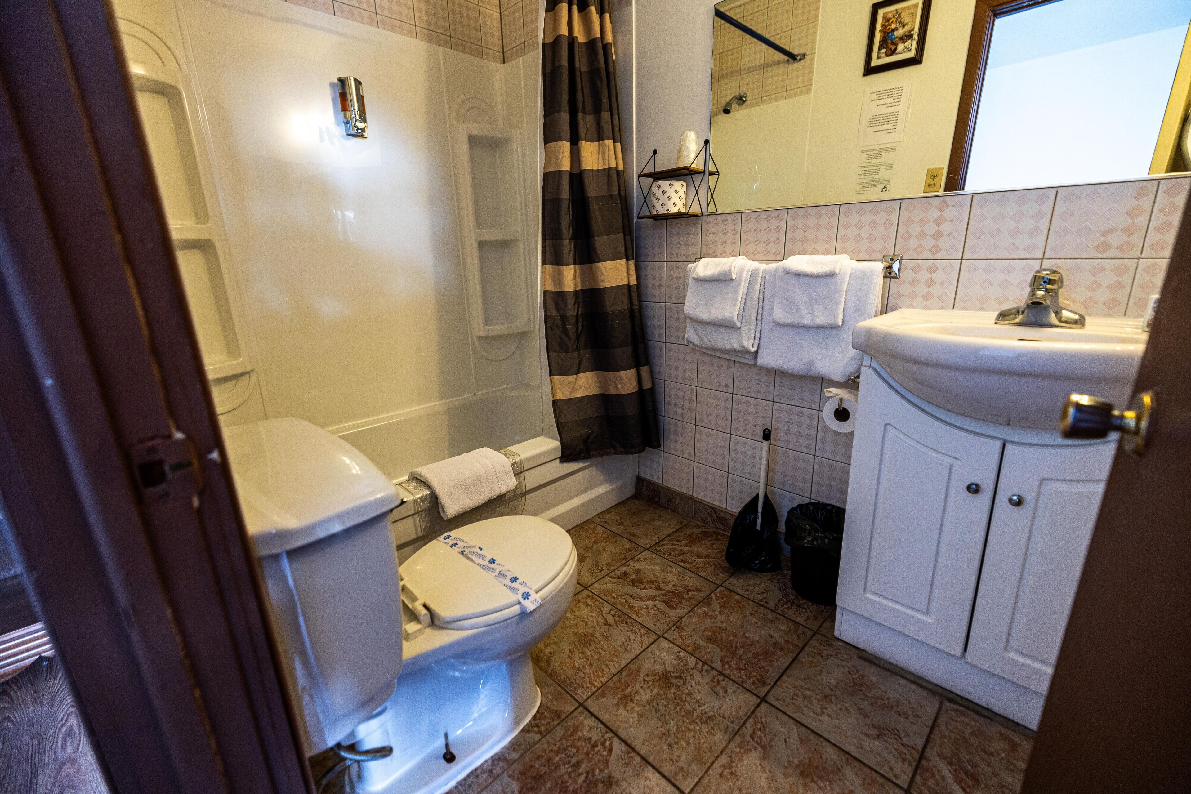 A bathroom with a toilet, bathtub, shower curtain, sink, and a mirror.