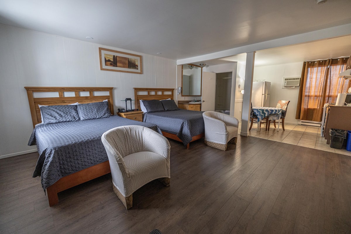 Hotellihuone, jossa on kaksi sänkyä, oleskelualue pöydällä ja tuoleilla sekä pieni keittiönurkkaus.