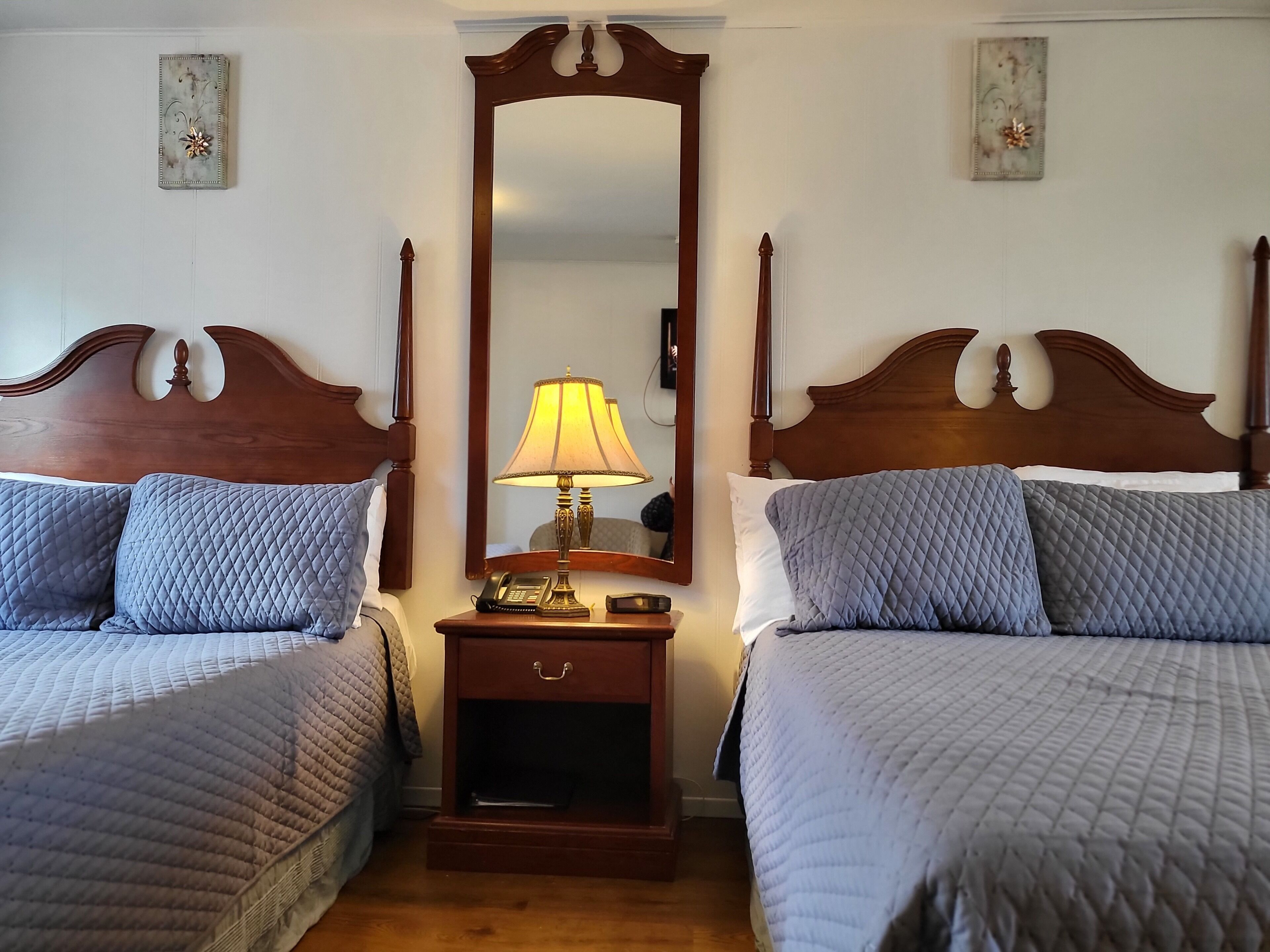 A hotel room with two beds, a nightstand with a lamp, and a mirror.