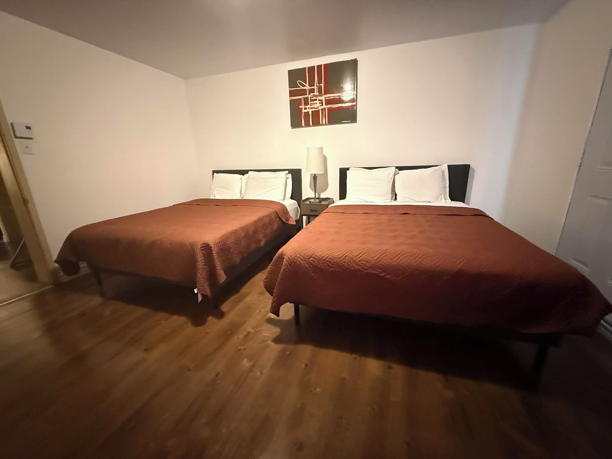 Ein Hotelzimmer mit zwei Einzelbetten, einem Nachttisch mit Lampe und einem an der Wand befestigten, abstrakten Kunstwerk.