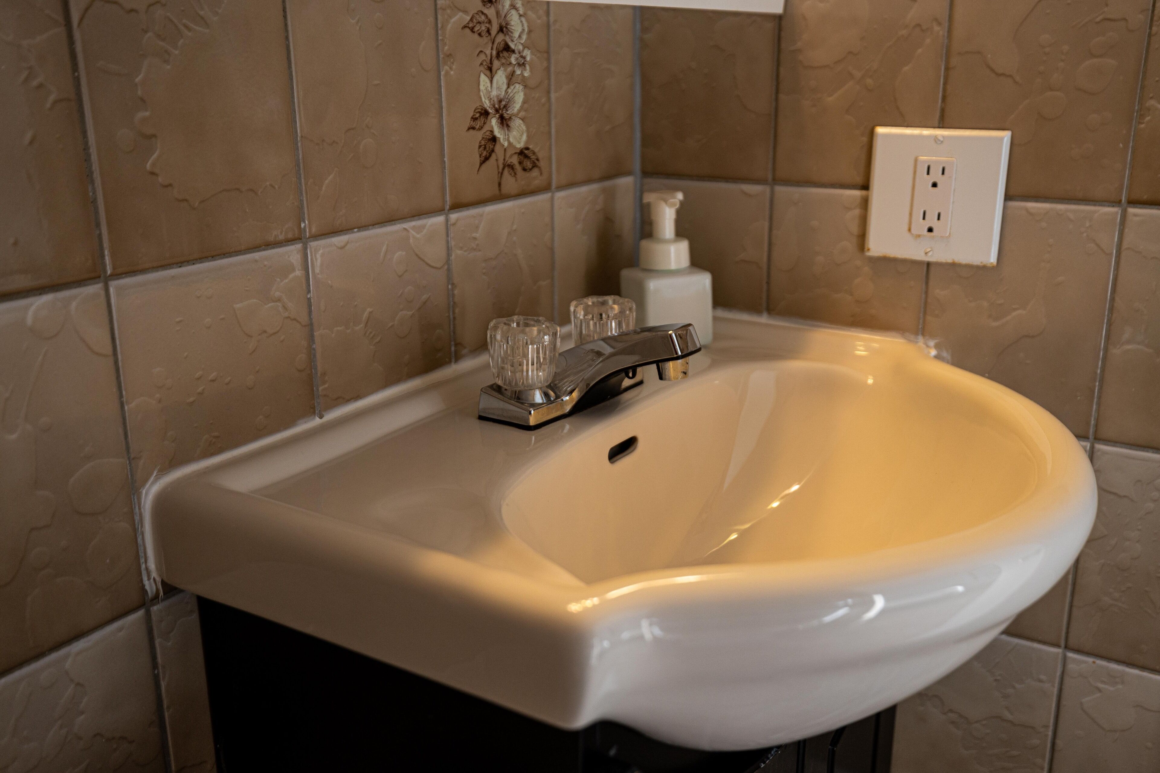 A bathroom sink with a faucet, a soap dispenser, and a glass on the countertop.