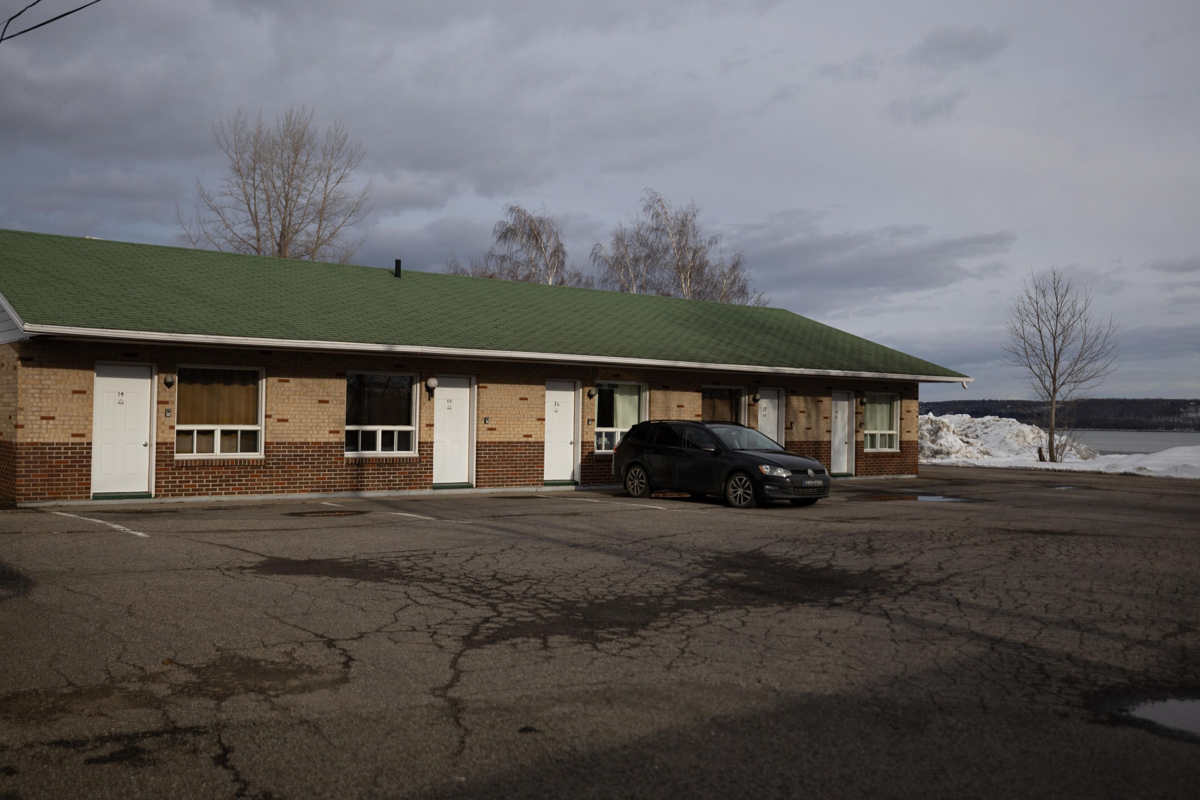 A motel with a green roof, brick exterior, and a parked car in front.