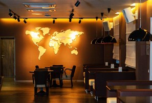 A restaurant interior with a world map on the wall, tables, chairs, and pendant lighting. - Chagala Hotel Bautino (Fort Shevchenko)