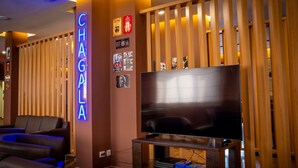 Un soggiorno moderno con una TV a schermo piatto su un supporto in legno, divani in pelle e un neon con la scritta "CHAGALLA".