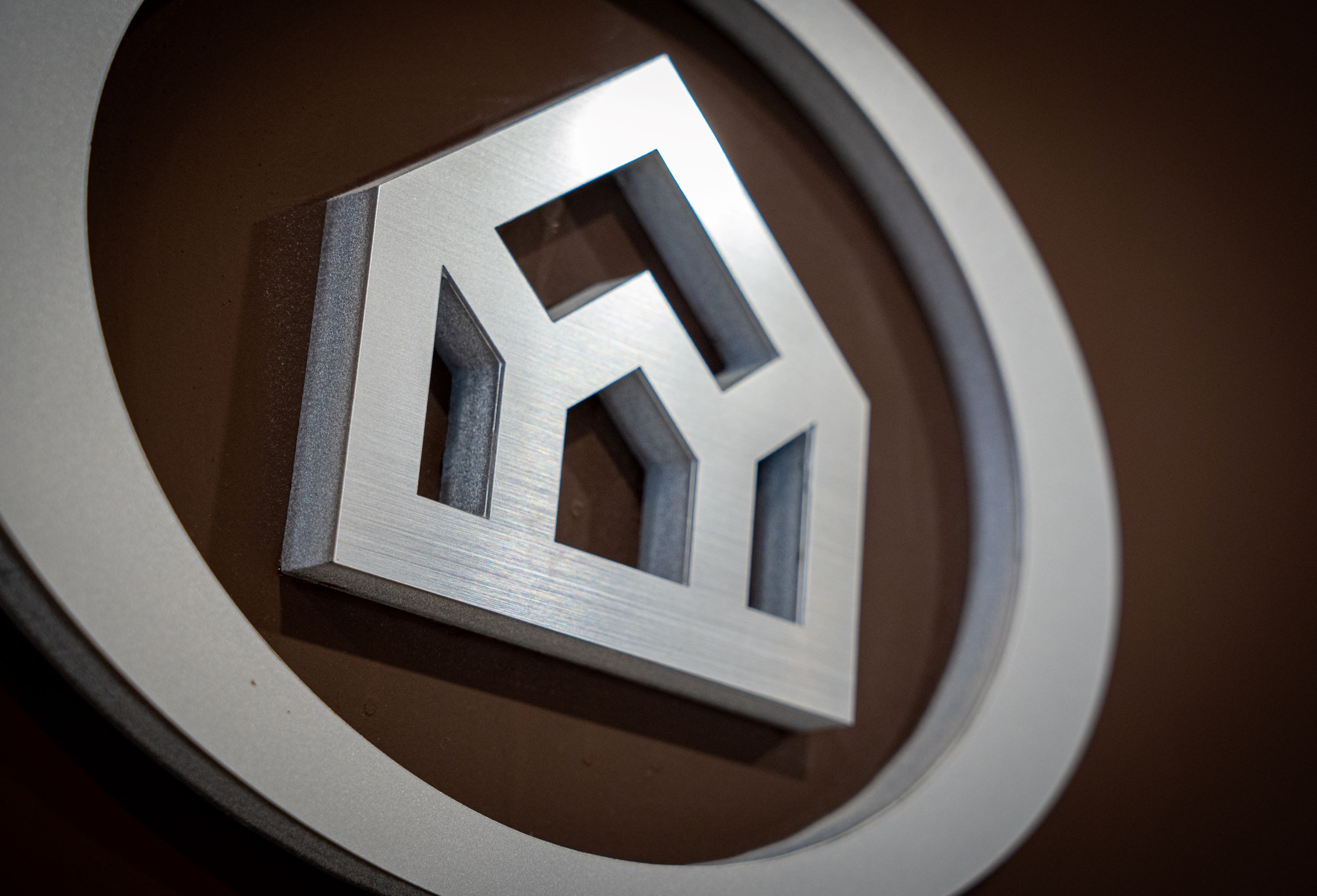 Un logo métallique aux formes géométriques, sur un fond circulaire.