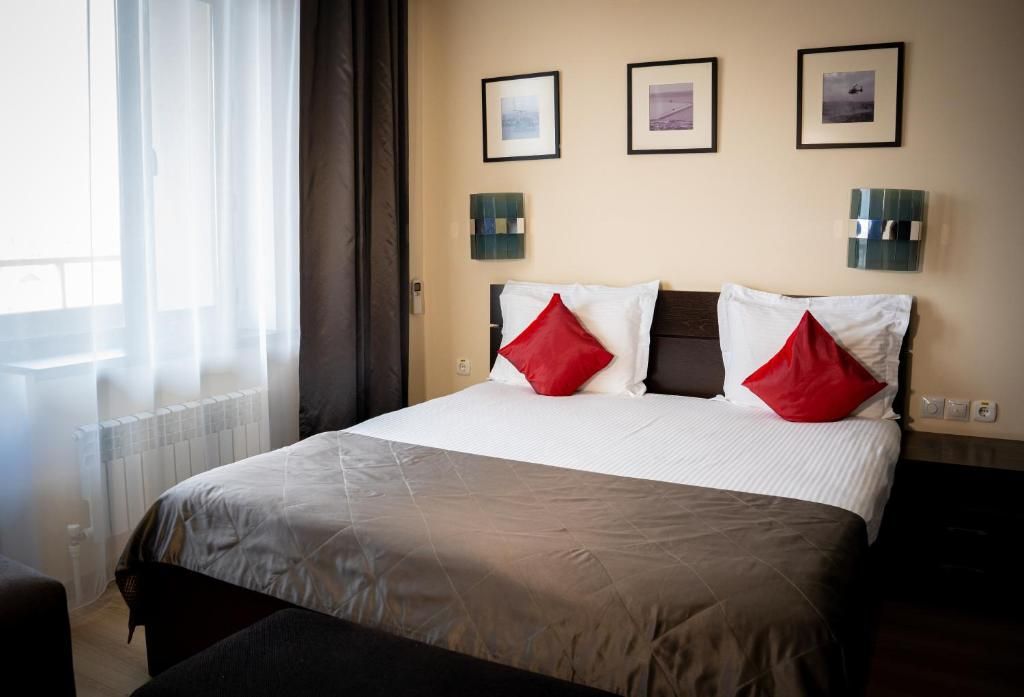 A hotel room with a bed, a window with curtains, and wall-mounted lights.