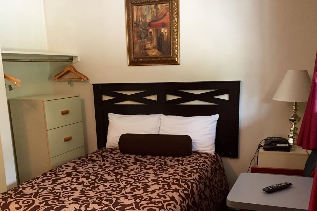 Habitación de hotel con cama, escritorio, silla, lámpara y un cuadro en la pared.