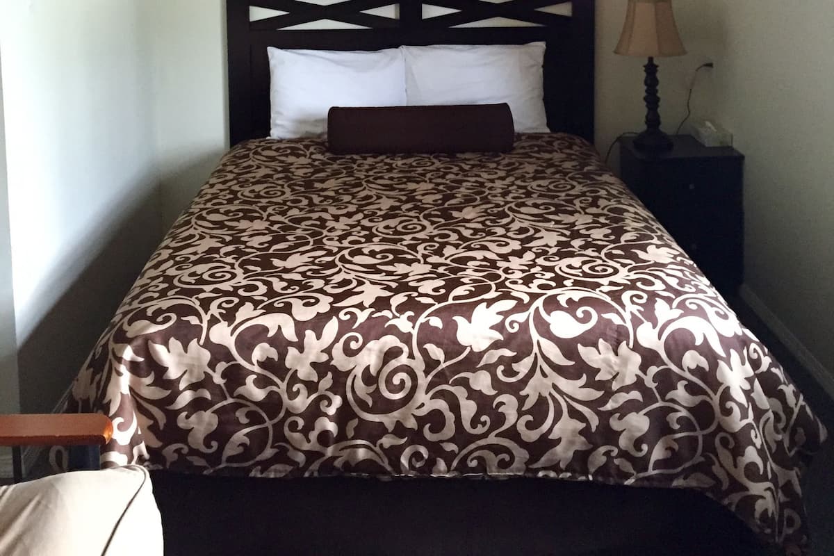 Un dormitorio con cama, ventilador de techo, mesita de noche, lámpara y un cuadro en la pared.