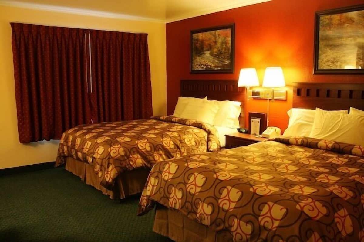 Habitación de hotel con dos camas, un ventanal con cortinas rojas, dos lámparas de pared y dos cuadros.