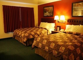 Habitación de hotel con dos camas, un ventanal con cortinas rojas, dos lámparas de pared y dos cuadros.