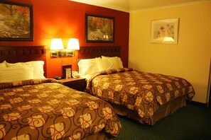 A hotel room with two beds, a nightstand with a lamp, and two framed pictures on the wall.