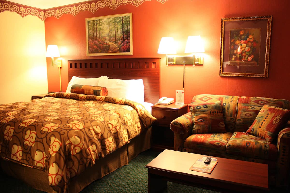 Habitación de hotel con una cama grande, un sofá, una mesita de noche y dos lámparas de pared.