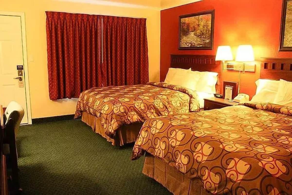 Una habitación de hotel con dos camas, un ventanal con cortinas rojas, un cuadro en la pared y una mesita de noche con lámparas.