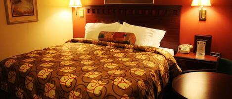 A hotel room with a large bed, two bedside lamps, a bedside table with a telephone, and a framed picture on the wall.