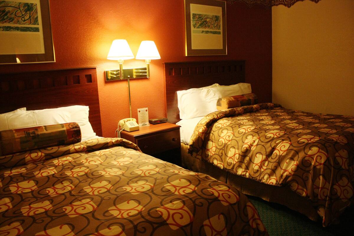 Habitación de hotel con dos camas, cada una con ropa de cama estampada, una mesita de noche con teléfono y lámparas de pared.