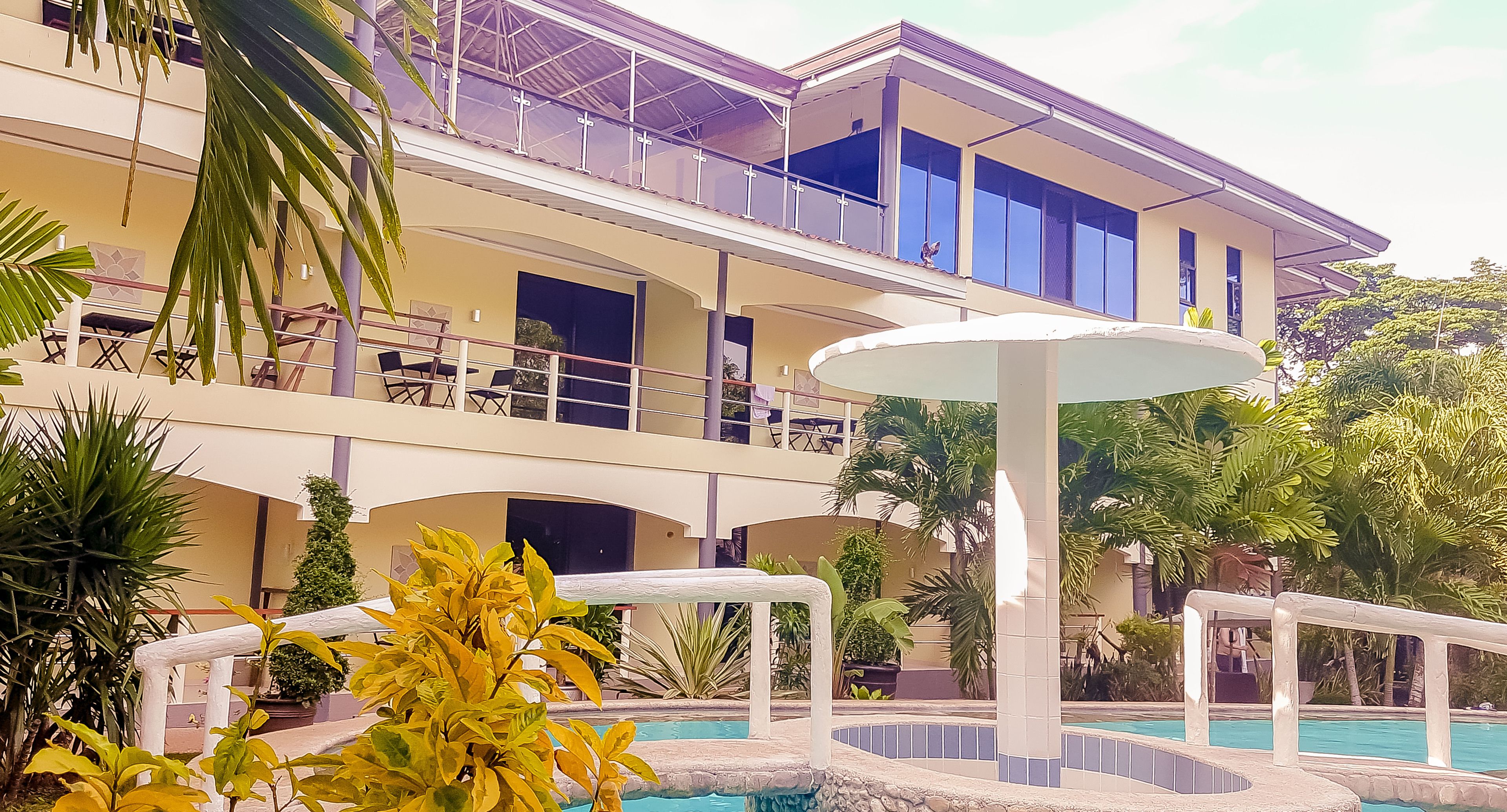 A multi-story hotel with balconies, a swimming pool, and tropical landscaping.