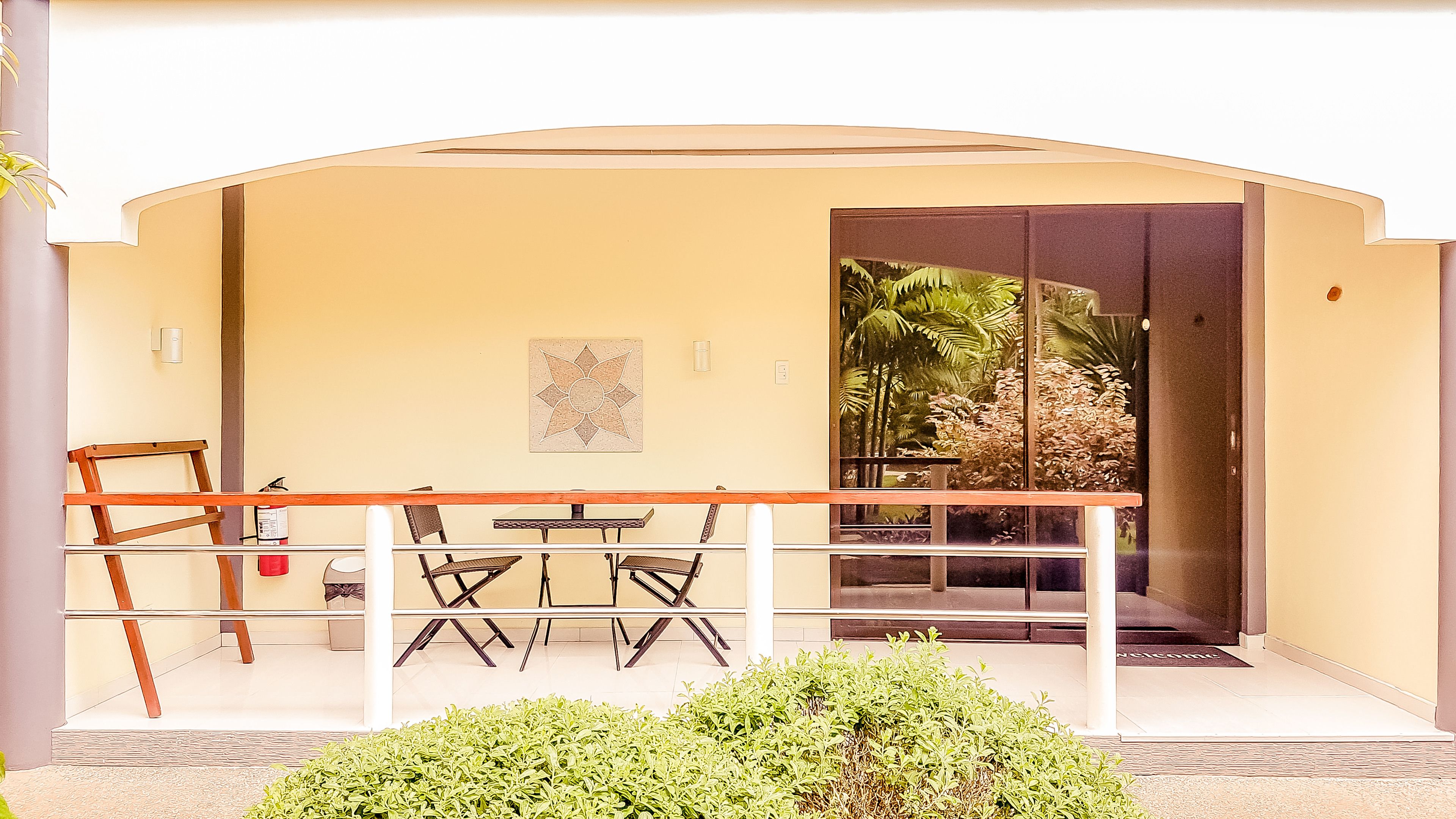 A balcony with a table and chairs, a wooden chair, a small table with a box, and a plant.