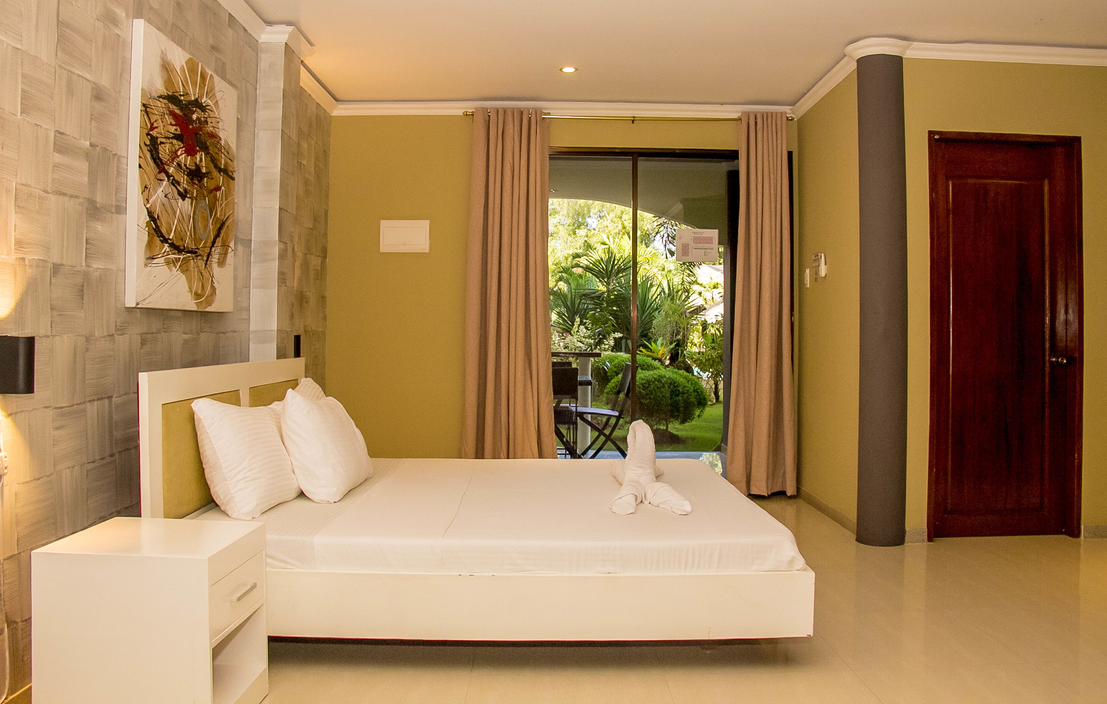 Una habitación de hotel moderna con una cama grande, una mesita de noche, una obra de arte colgada en la pared y vistas a zonas verdes por la ventana.