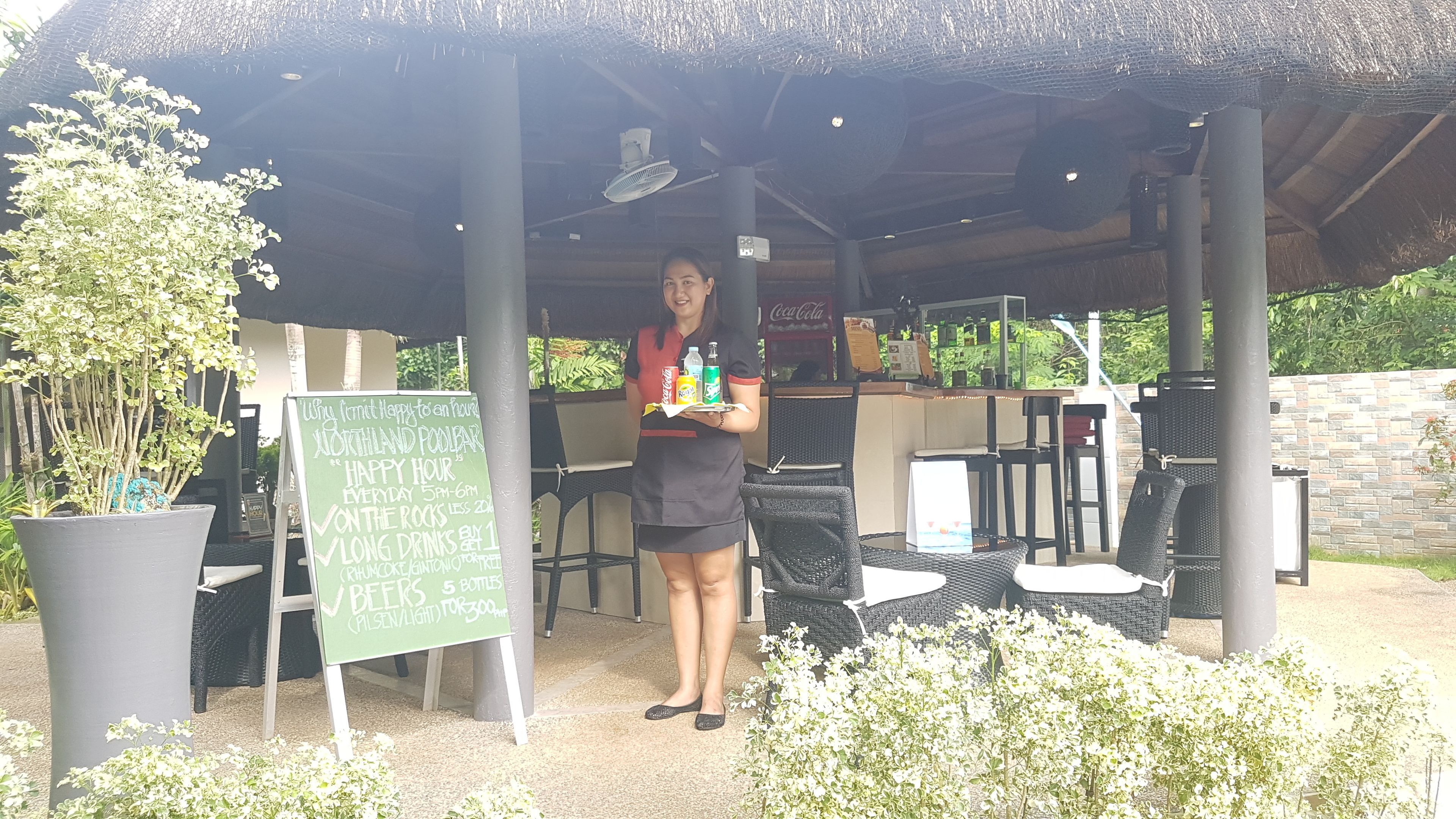 A person standing under a covered outdoor area with a signboard advertising a happy hour offer.
