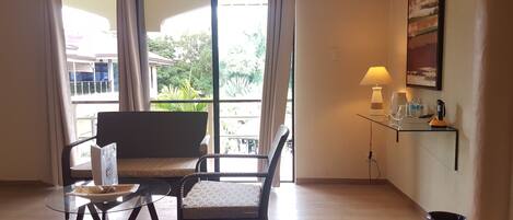 A room with a sofa, a glass table, a lamp, and a view of greenery outside.