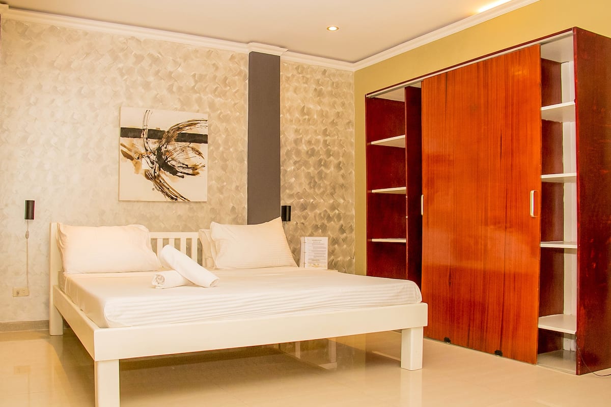 A bedroom with a bed, a wooden wardrobe, and a wall-mounted artwork.