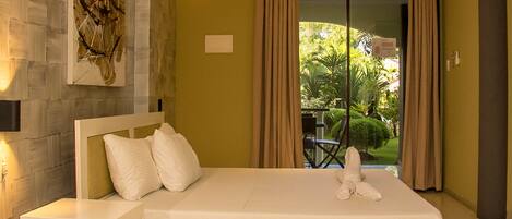 A hotel room with a large bed, a nightstand, a wall-mounted artwork, and a view of a garden through a sliding door.
