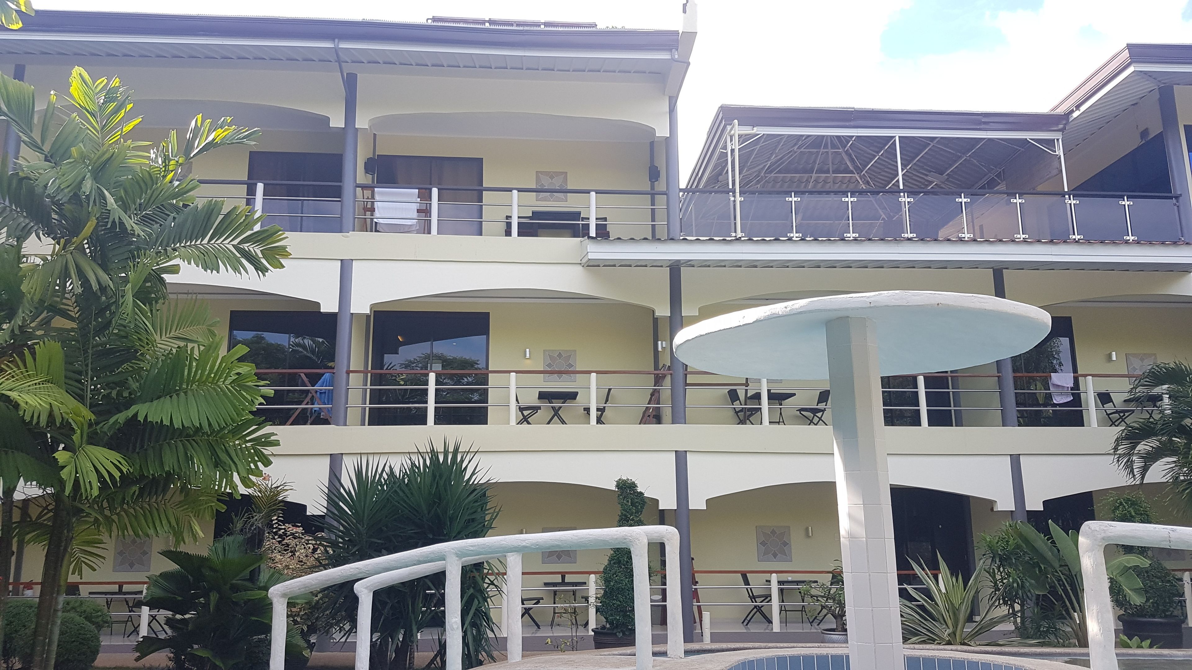 Un immeuble à plusieurs étages doté de balcons, d’un espace extérieur aménagé pour s’asseoir et d’une fontaine ou d’un élément décoratif aquatique central.