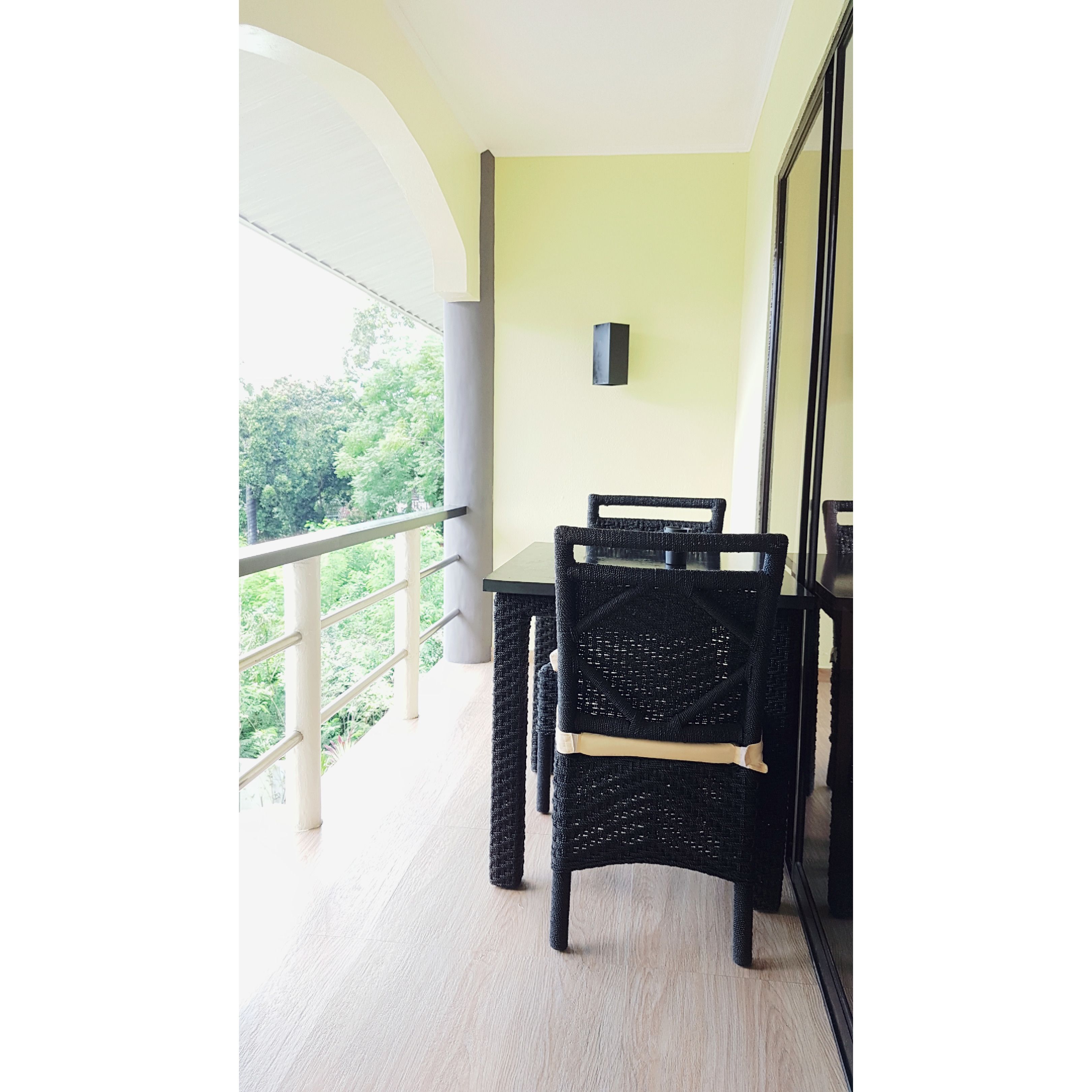 Un balcón con una mesa y sillas, vistas a zonas verdes y una lámpara fijada a la pared.