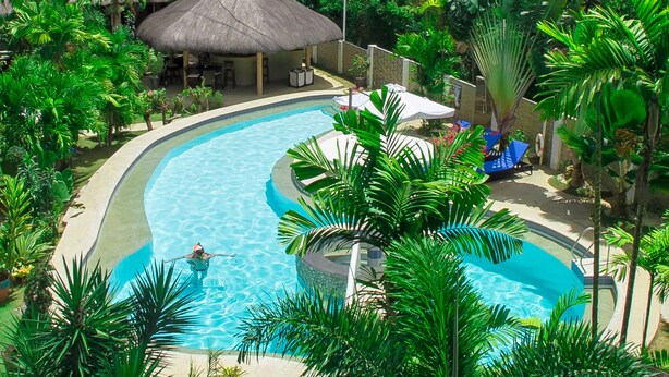 Ett semesterparadis med en stor swimmingpool omgiven av frodig grönska och byggnader med halmtak.