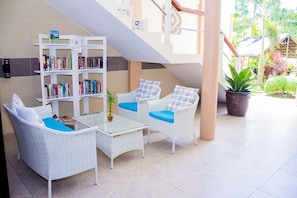 Un coin lecture aménagé avec des meubles en osier, une bibliothèque et un escalier.