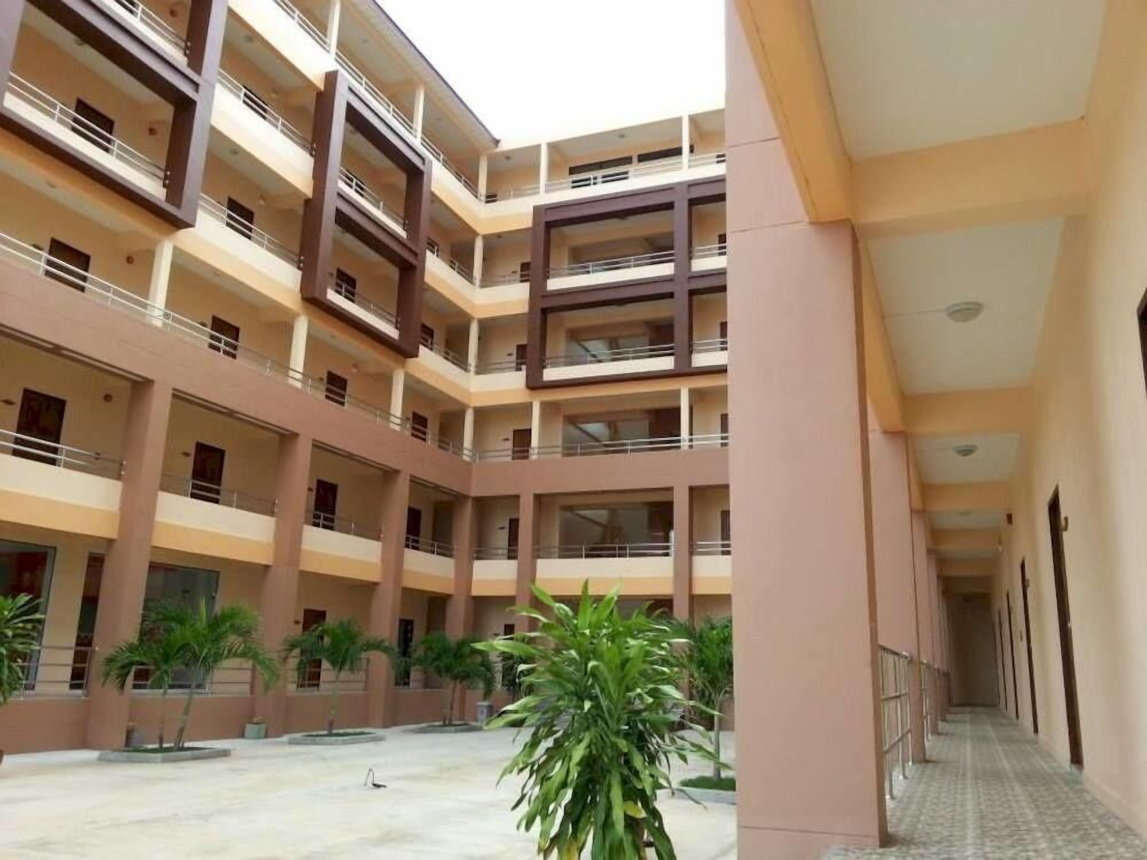 A multi-level building with balconies, a central courtyard with palm trees, and a tiled floor.