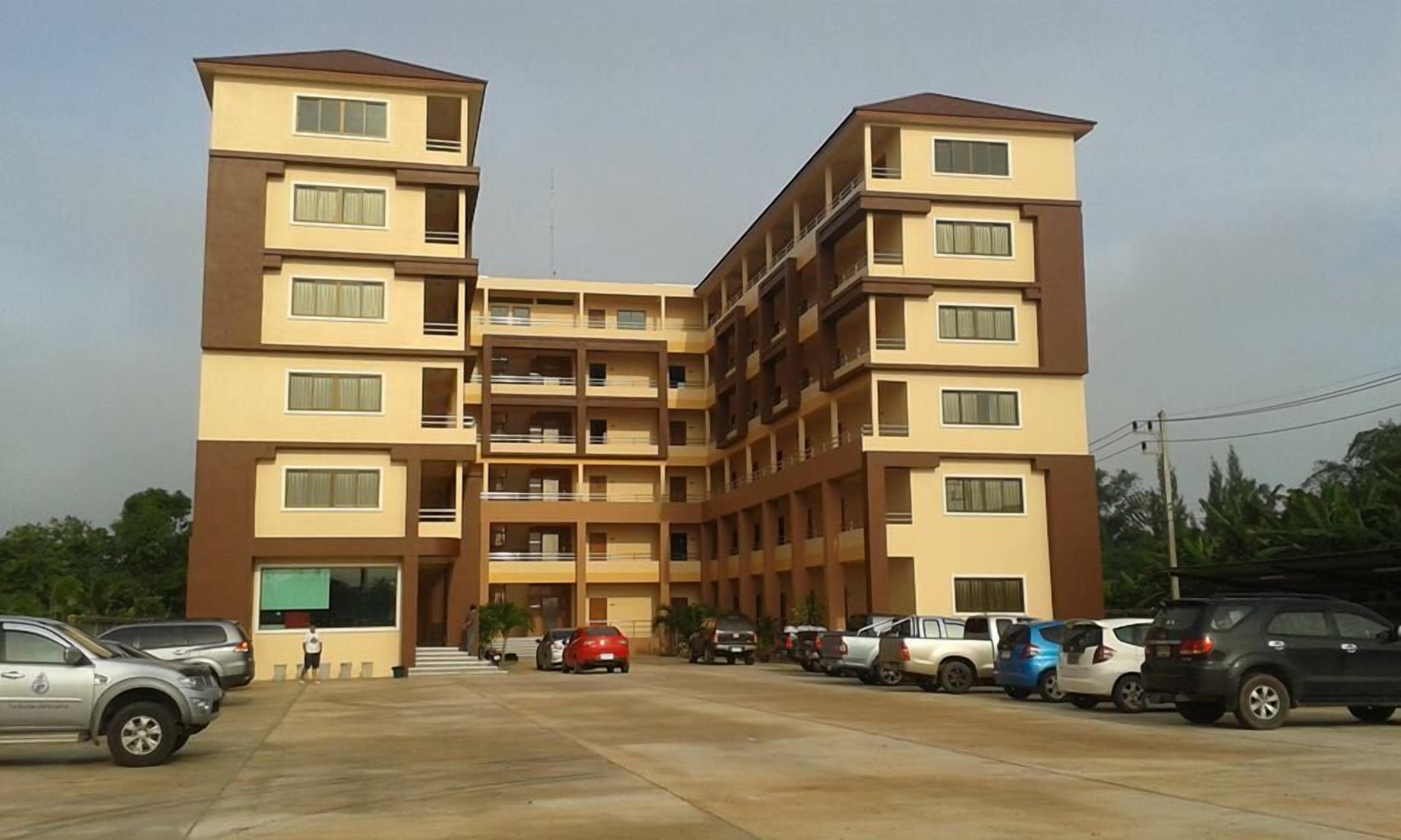 Un edificio residencial de varios pisos con un patio central, balcones y un área de estacionamiento con varios automóviles.