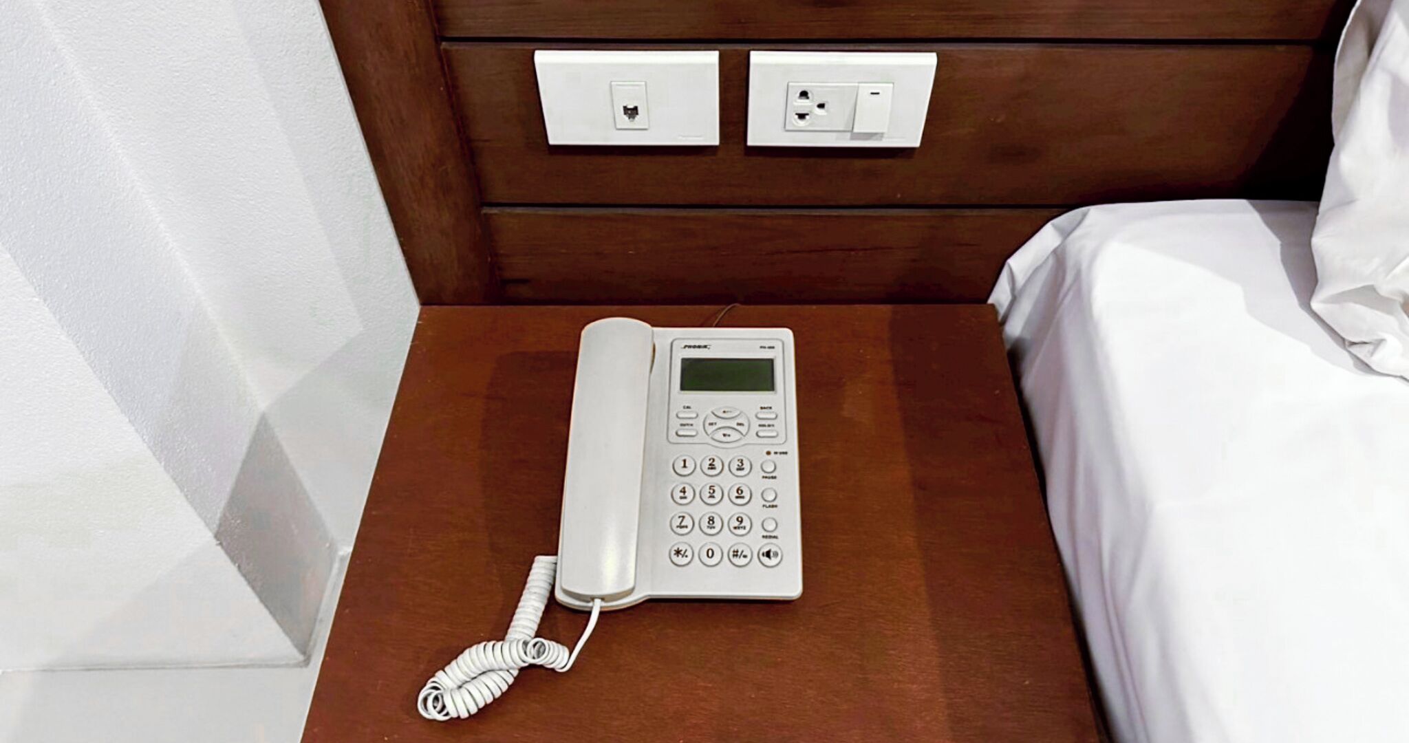 A hotel room with a bedside phone on a wooden nightstand.