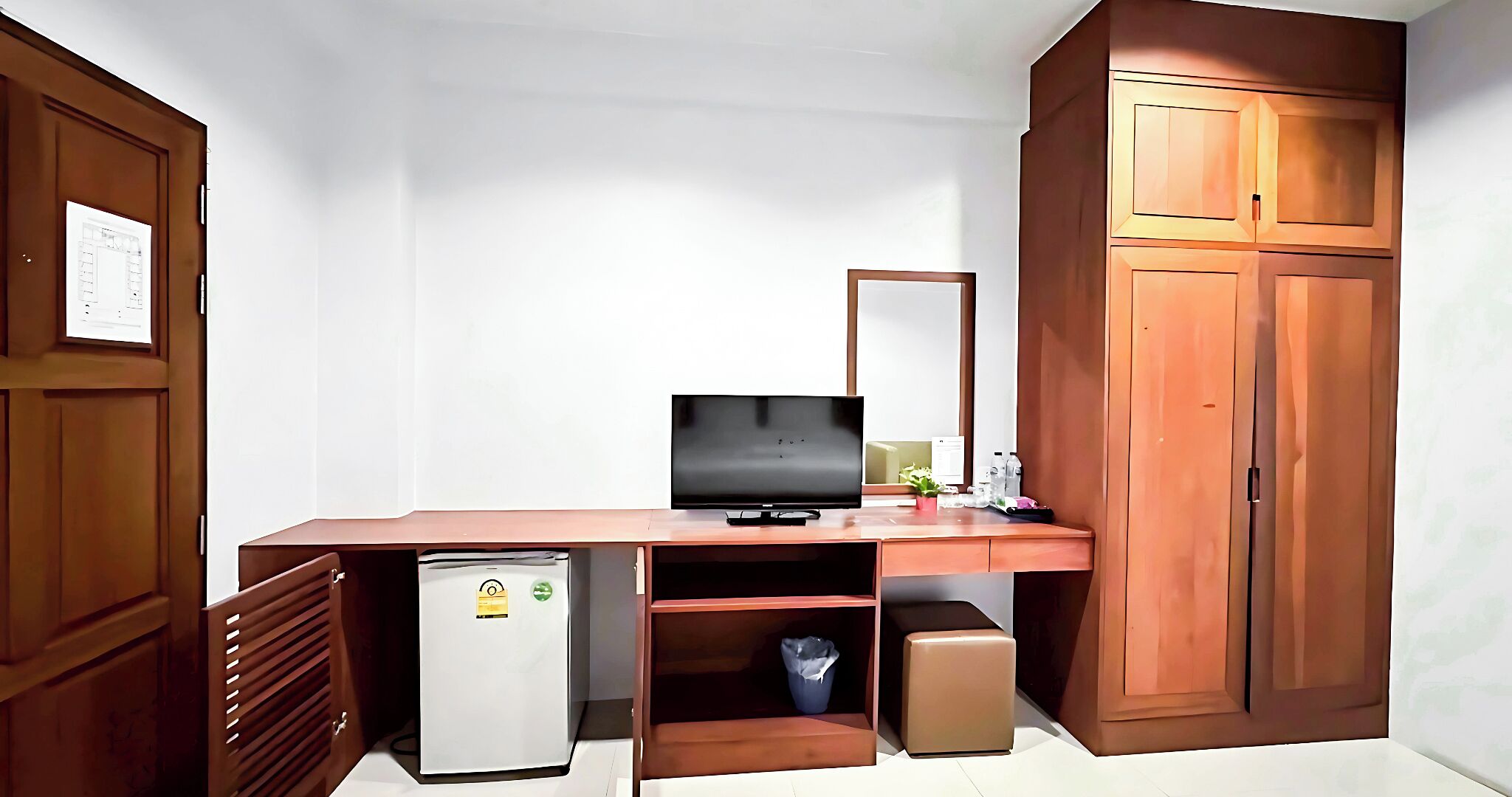 A compact room with a wooden desk, a television, a small refrigerator, and a cabinet.