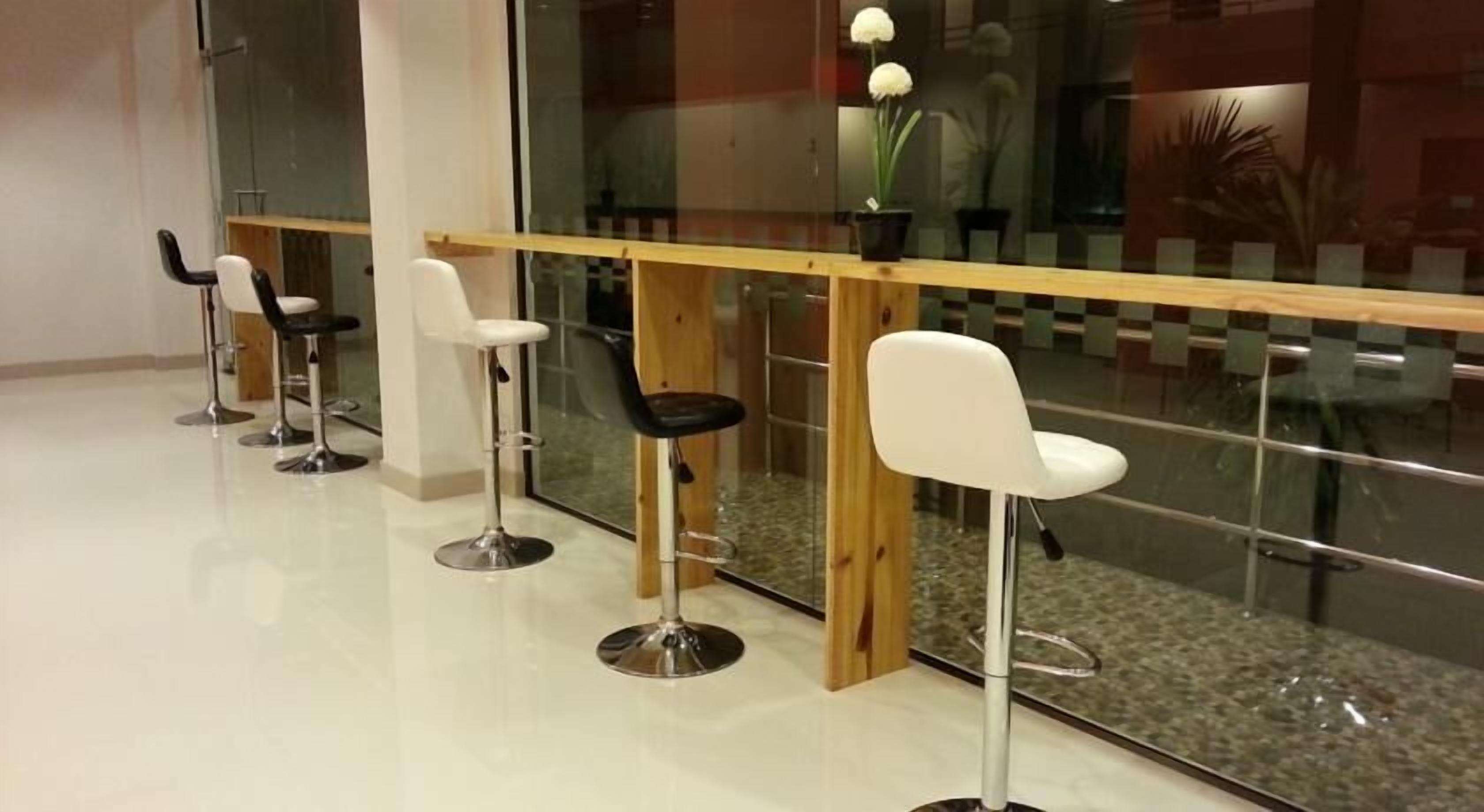 A modern bar area with white and black bar stools, a wooden bar counter, and a glass partition.