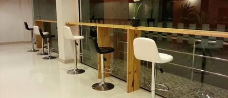 Un área de bar moderna con taburetes blancos y negros, una barra de madera y un separador de vidrio.