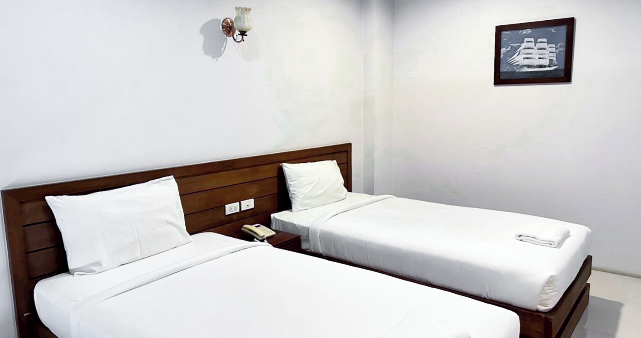 Una habitación de hotel con dos camas individuales, un cabecero de madera, una mesita de noche con teléfono y un cuadro en la pared.
