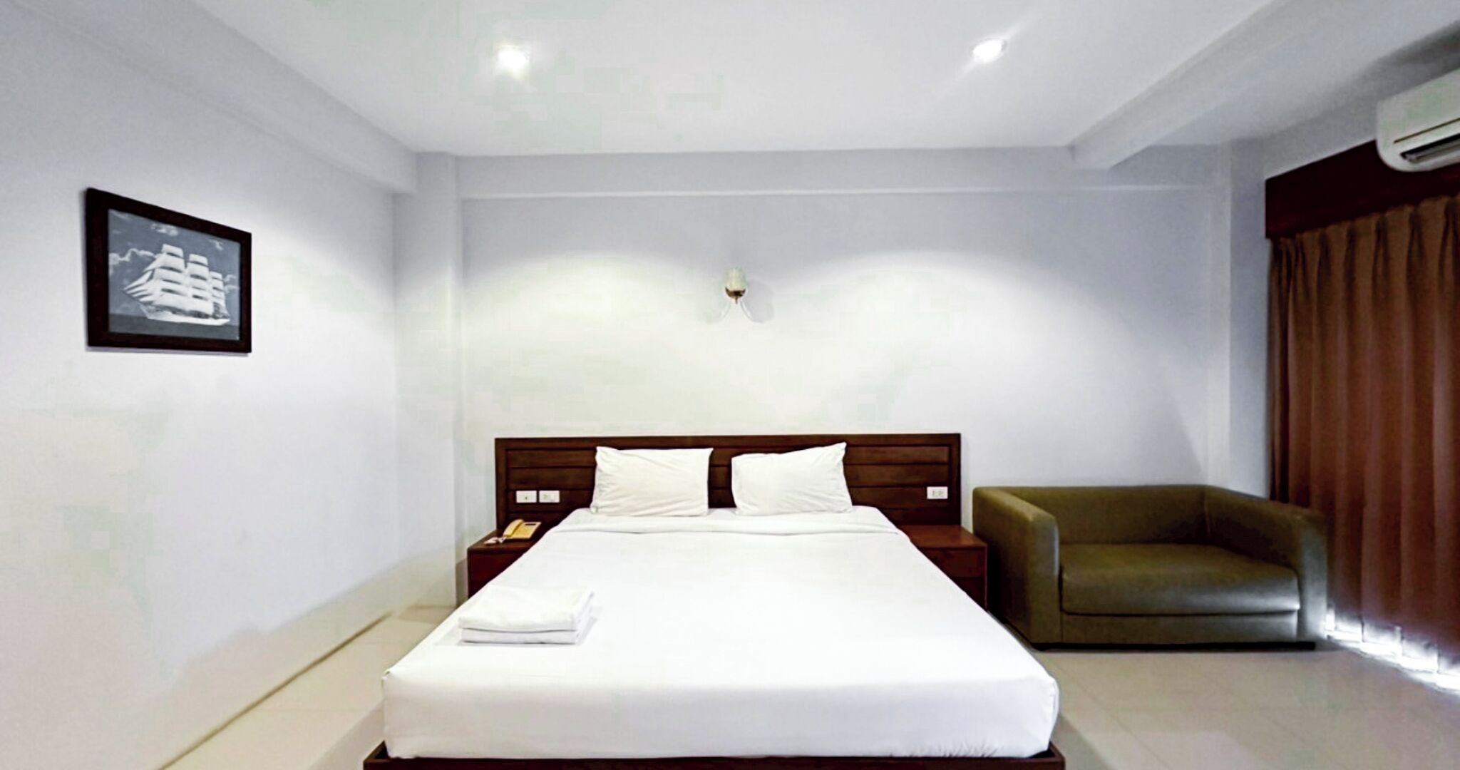 A hotel room with a large bed, a nightstand, a green armchair, and a wall-mounted light fixture.