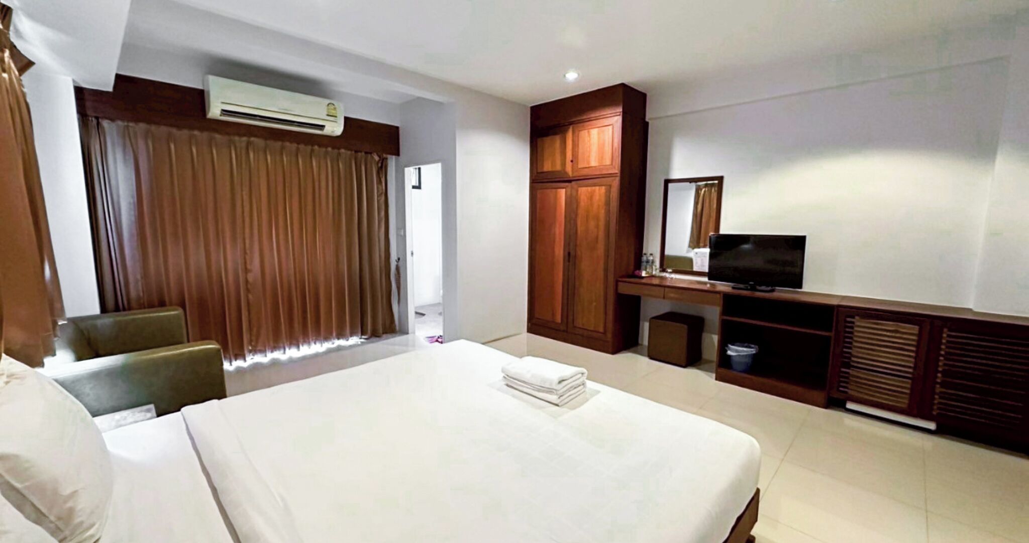 A hotel room with a bed, a desk with a TV, a chair, a wardrobe, and an air conditioning unit.