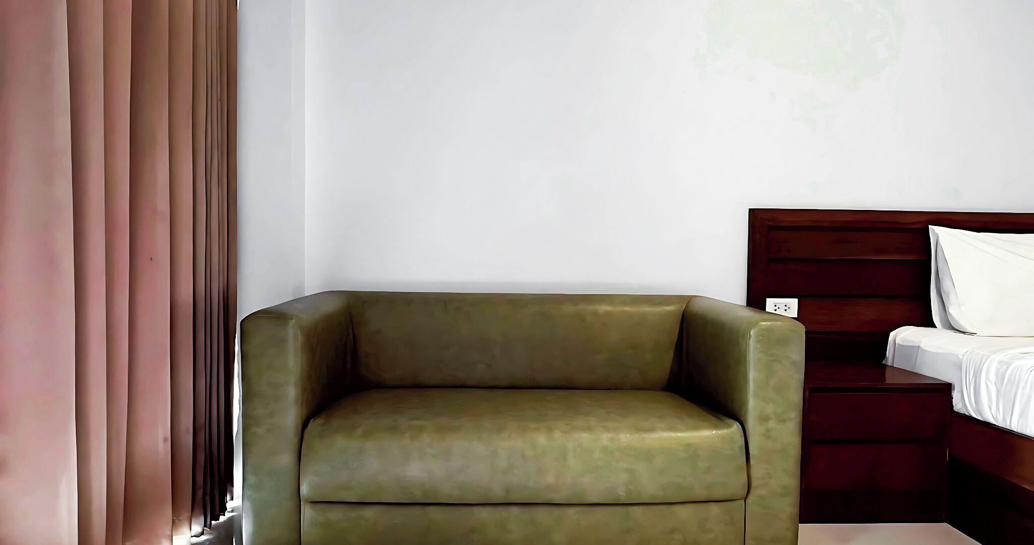 A room with a green armchair, a wooden bed with white bedding, and a white wall.