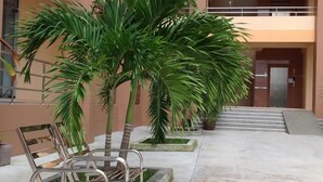 Un edificio con una escalera que lleva a un nivel superior, rodeado de plantas en macetas y sillas de metal.